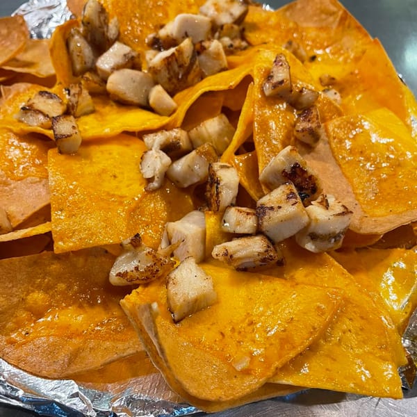 Close-up of Sam's Burger Deli's cheesy nachos topped with grilled chicken pieces, served in foil.