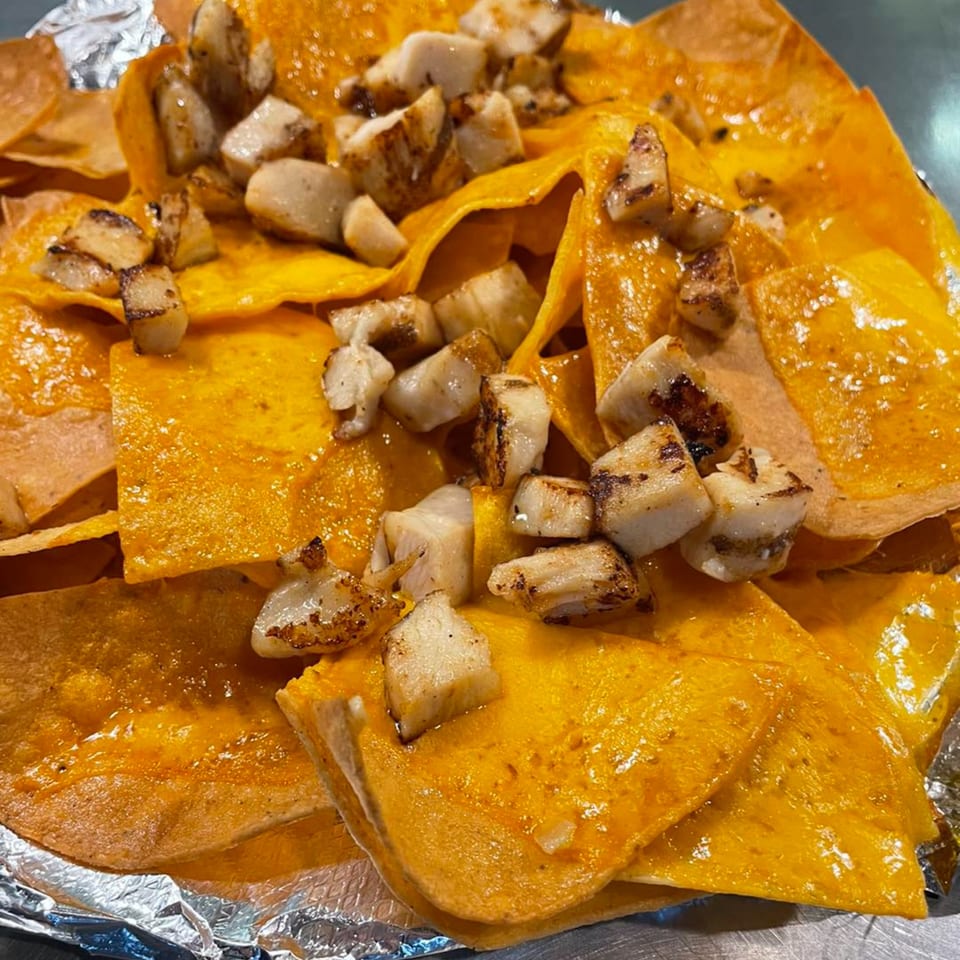 Close-up of Sam's Burger Deli's cheesy nachos topped with grilled chicken pieces, served in foil.
