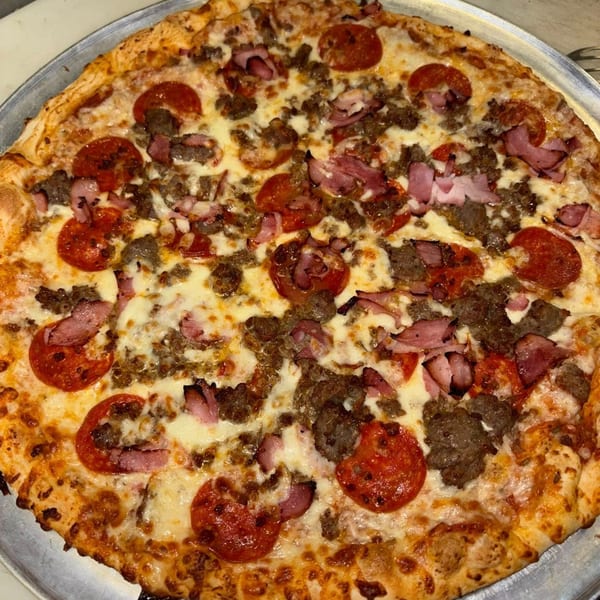 A large, round meat lover's pizza with pepperoni, sausage, and ham on a metal tray.