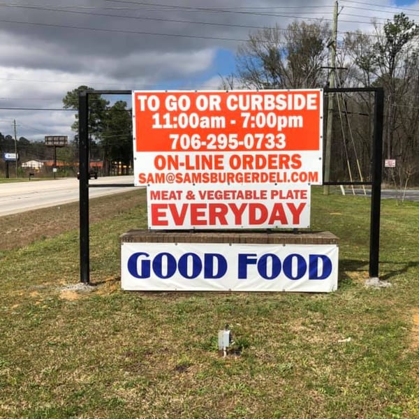 Sam's Burger Deli sign advertising to-go, curbside, online orders, and meat & vegetable plates.