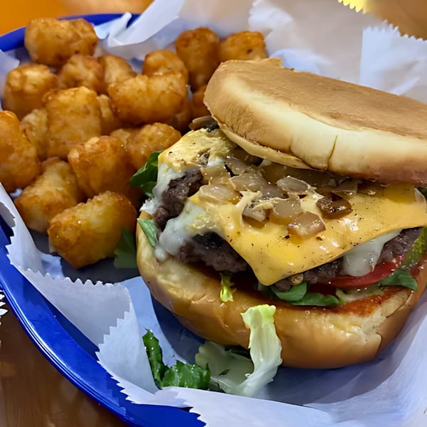 A Sam's Burger Deli cheeseburger with caramelized onions and tater tots in a blue basket.