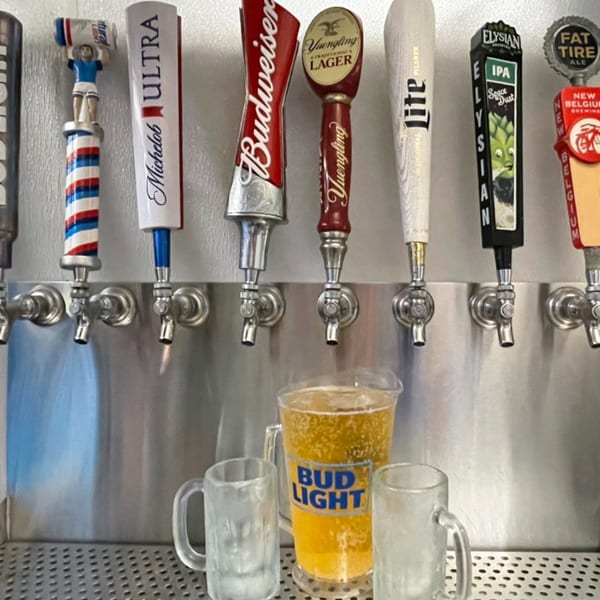 A row of beer taps with various brand handles, a pitcher of beer, and two frosted mugs.