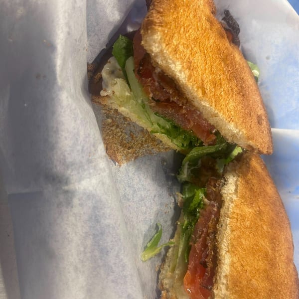 A toasted sandwich with lettuce, tomato, and bacon, cut in half and wrapped in white paper.