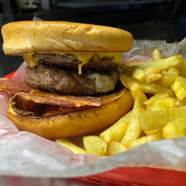 Double cheeseburger with bacon and fries in a red basket from Sam's Burger Deli.