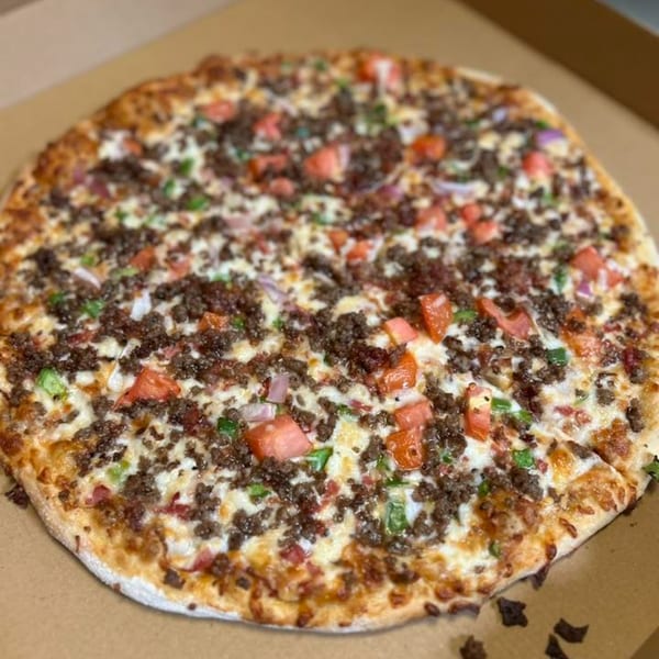 A whole pizza with ground beef, diced tomatoes, green peppers, and onions in a cardboard box.