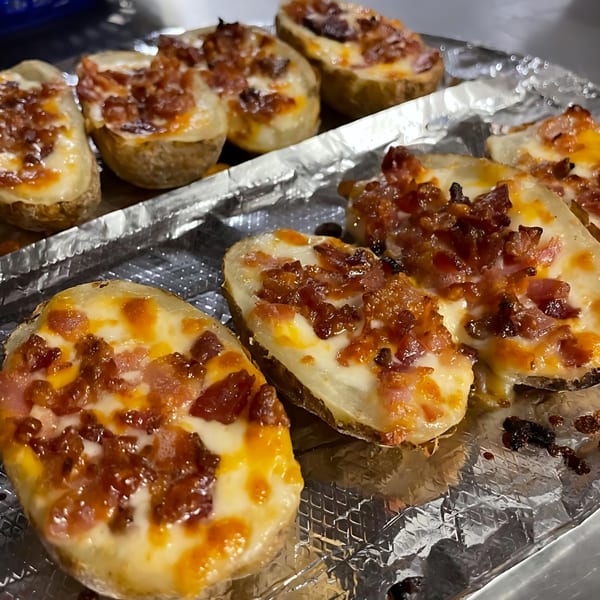Close-up of several loaded potato skins with melted cheese and bacon bits on aluminum foil.
