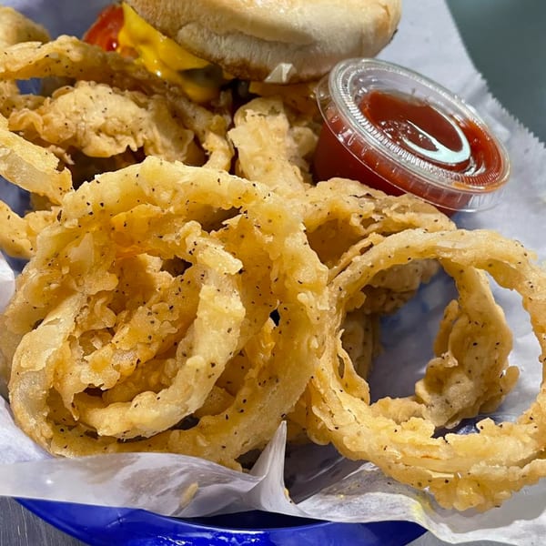 Crispy golden onion rings with black pepper, a burger, and a side of ketchup in a blue basket.