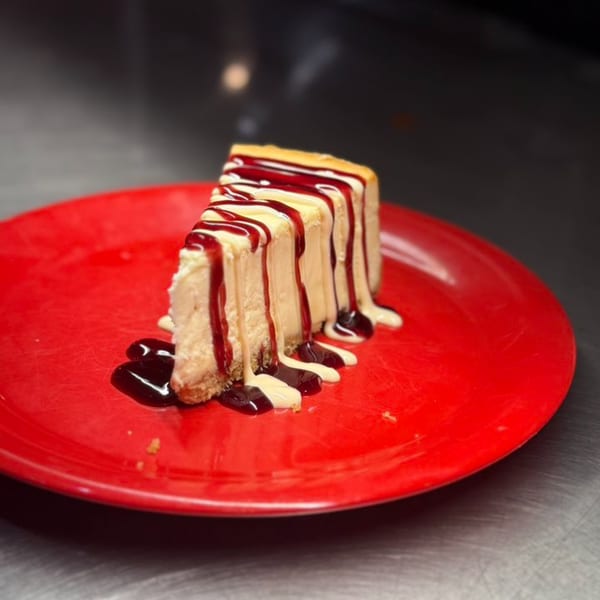 A slice of cheesecake with raspberry and white chocolate drizzle on a red plate.