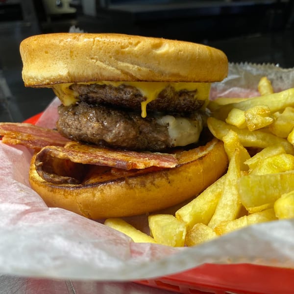 A double cheeseburger with bacon and melted cheese, served with golden french fries in a red basket.