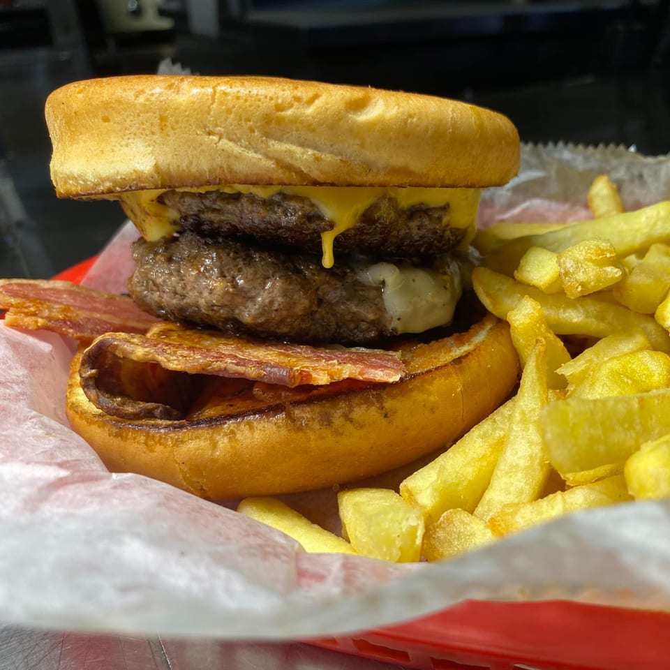A double cheeseburger with bacon and melted cheese, served with golden french fries in a red basket.