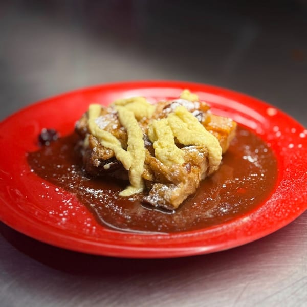 Bread pudding with yellow sauce, powdered sugar, and caramel on a red plate.