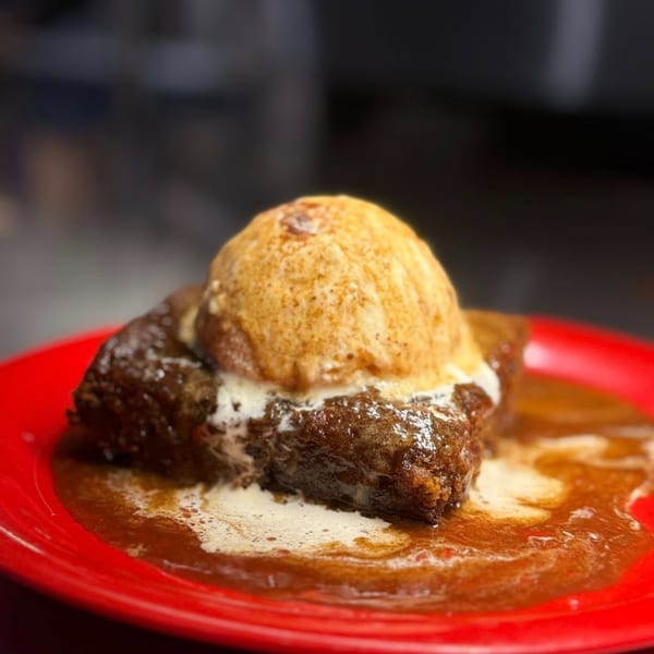 Warm brownie topped with a scoop of melting vanilla ice cream and caramel sauce on a red plate.