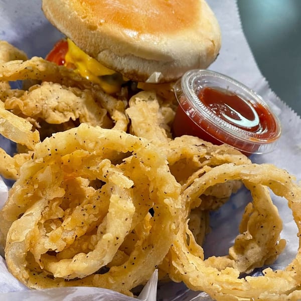 A burger with cheese and ketchup, alongside crispy onion rings and a side of ketchup.