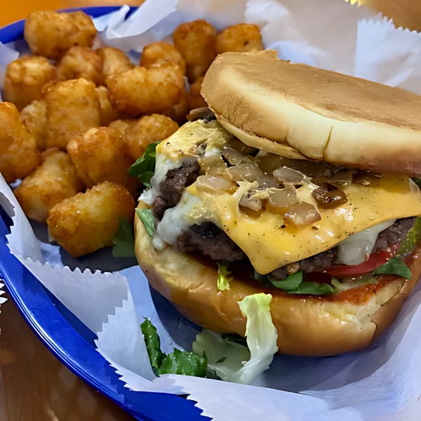 A Sam's Burger Deli cheeseburger with caramelized onions, lettuce, tomato, and a side of tater tots.