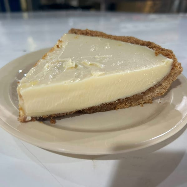 A slice of creamy white pie with a thick graham cracker crust on a light-colored plate.